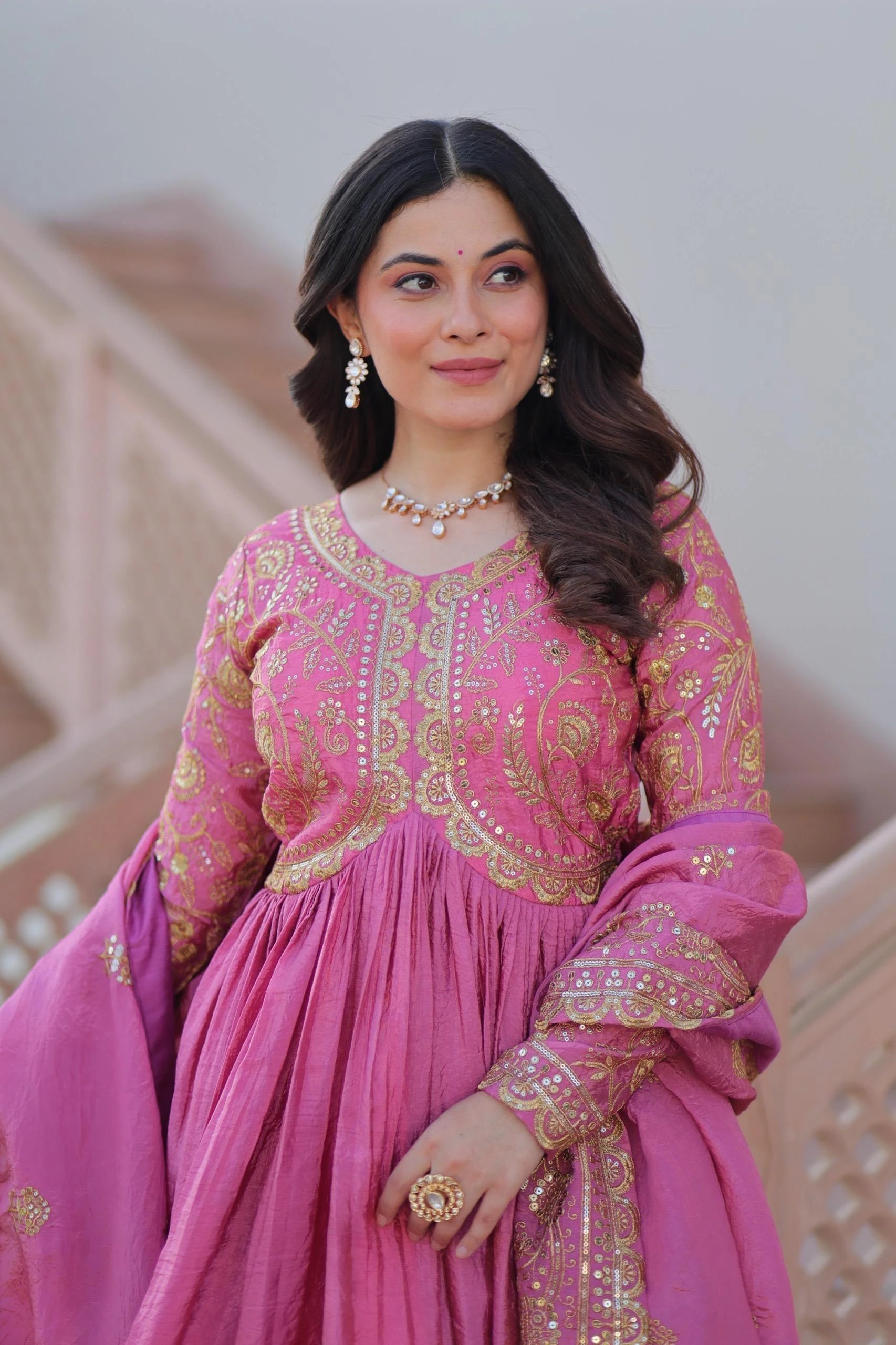 Woman in a pink traditional outfit with gold embroidery indoors.